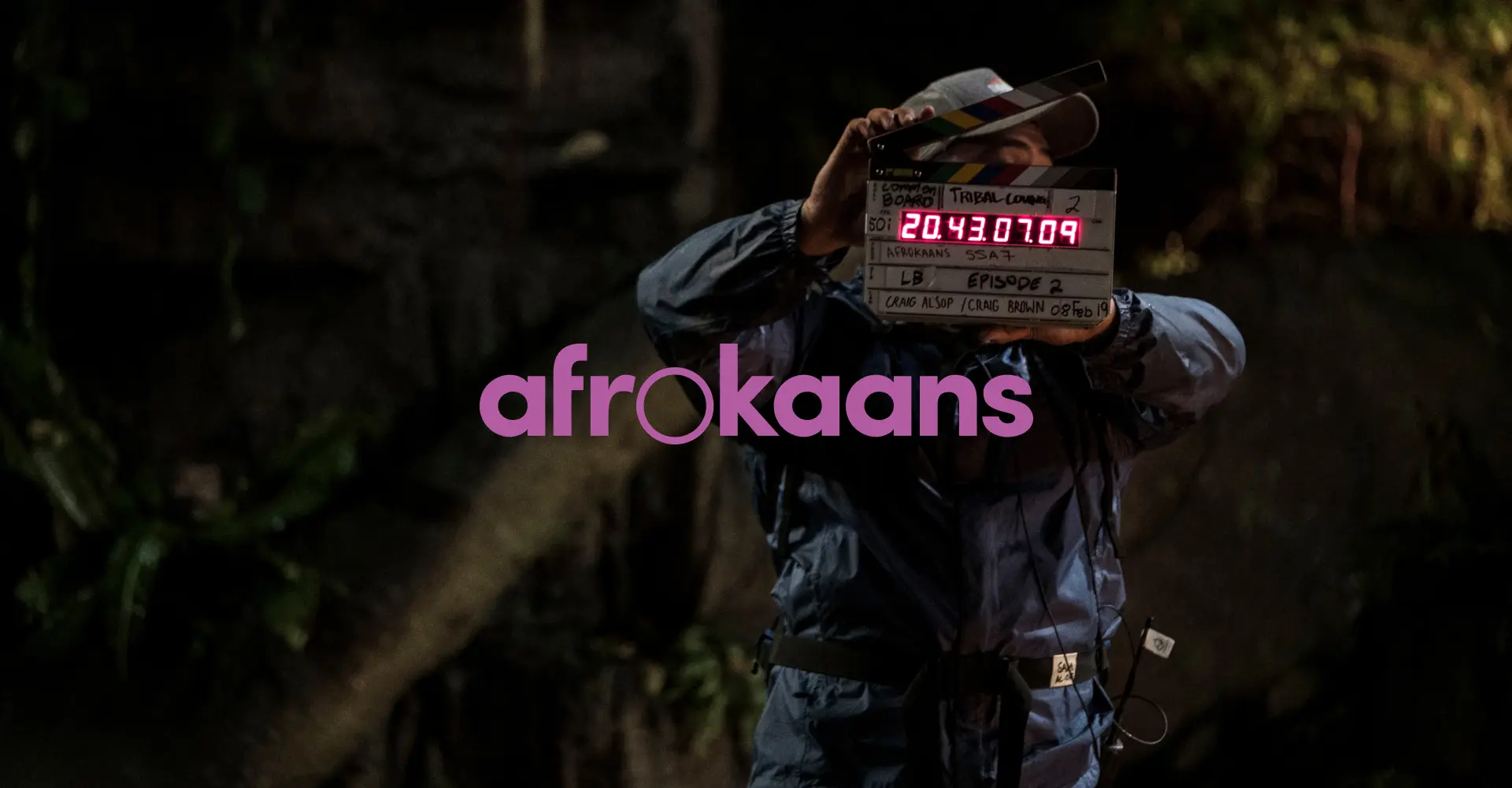 A person holding a movie clapperboard, with the word "afrokaans" displayed prominently in pink.