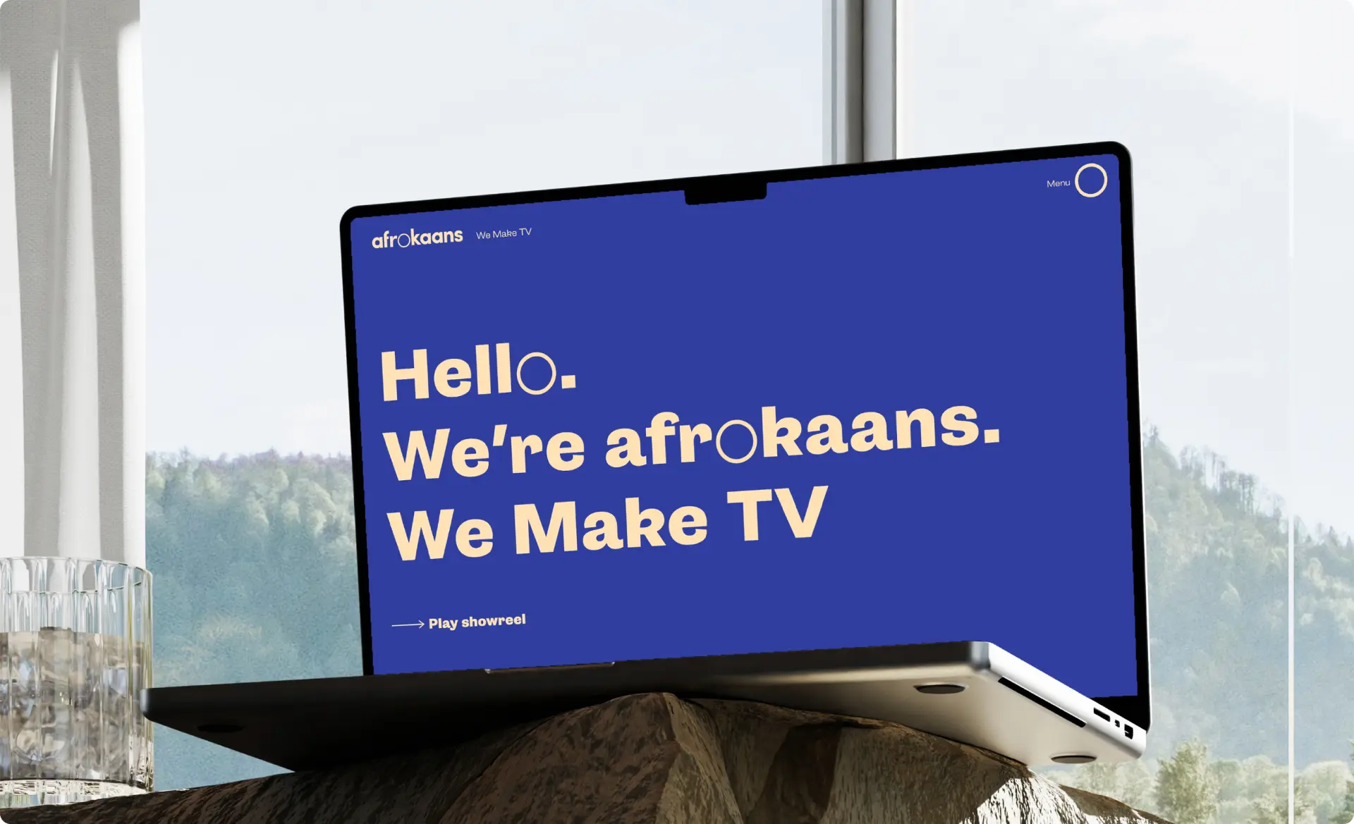 Laptop displaying a blue screen with the text "Hello. We're afrokaans. We Make TV." in a modern font.