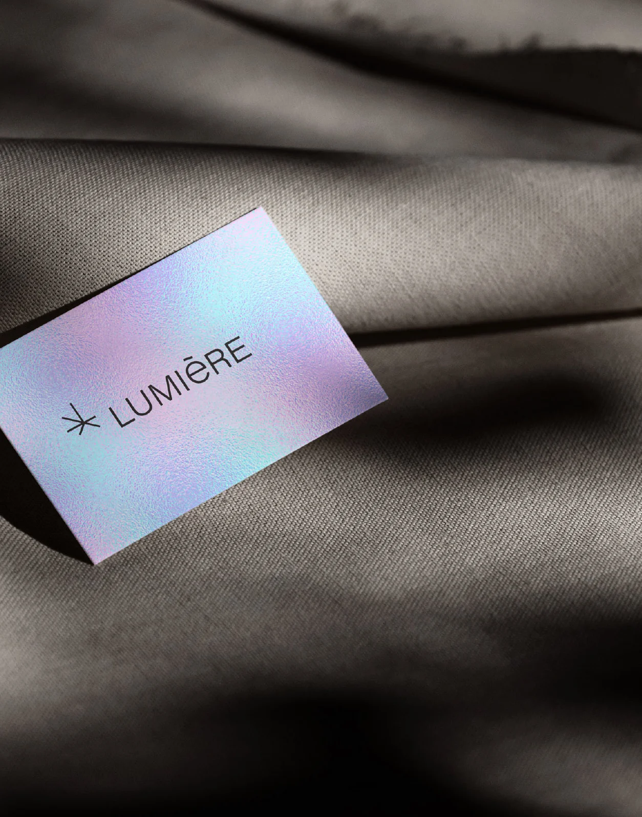 A business card with the text "LUMIÈRE" on a soft, neutral fabric background.