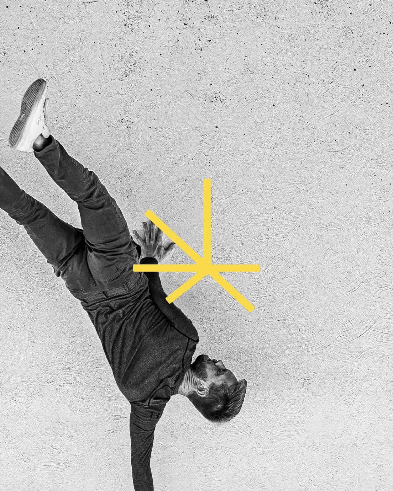A person performing a breakdance move against a textured wall, with a yellow geometric shape overlay.